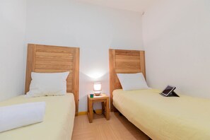 Ein Doppelzimmer mit zwei Betten, jedes mit einem Holz-Kopfstück, einem Nachttisch mit Lampe und einem Tablet auf einem Bett.