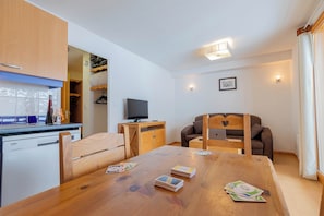 En kompakt bolig med tekøkken, et spisebord med spillekort, et fjernsyn og en sofa.