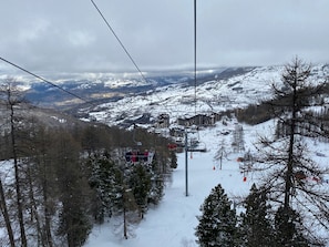 A ski lift with passengers, a snowy mountain landscape, and buildings in the background. - Appart cosy et charmant, coeur de la station (Les Orres)