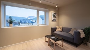 Una sala de estar moderna con un sofá, una mesa de centro y un ventanal con vistas a edificios y montañas.