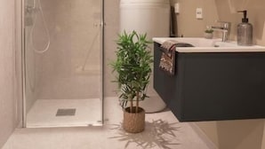 Un baño moderno con cabina de ducha de vidrio, inodoro redondo y tocador oscuro con espejo.