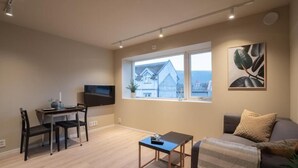 Una sala de estar con un sofá, una mesa de centro, un televisor y un ventanal con vistas a una casa.