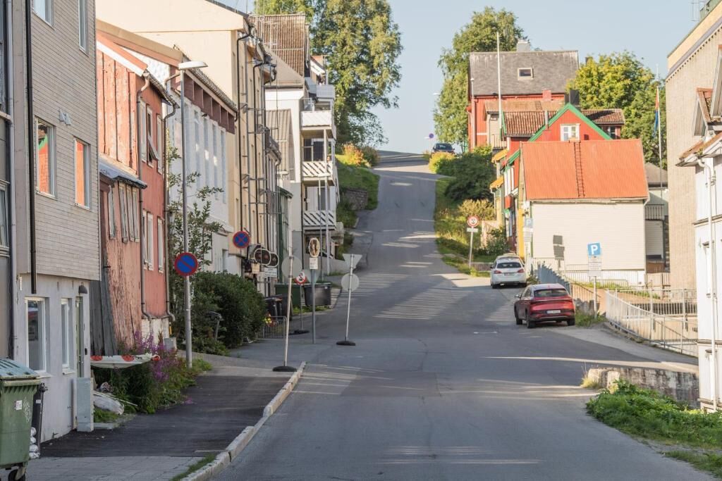Une rue résidentielle bordée de maisons des deux côtés, un ciel dégagé et une voiture garée sur le côté droit.