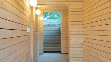 A narrow wooden hallway with a ceiling and walls made of horizontal wooden planks. There are three spherical light fixtures on the left wall.