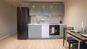 Una cocina compacta equipada con refrigerador, lavavajillas, horno y un comedor con mesa y sillas.