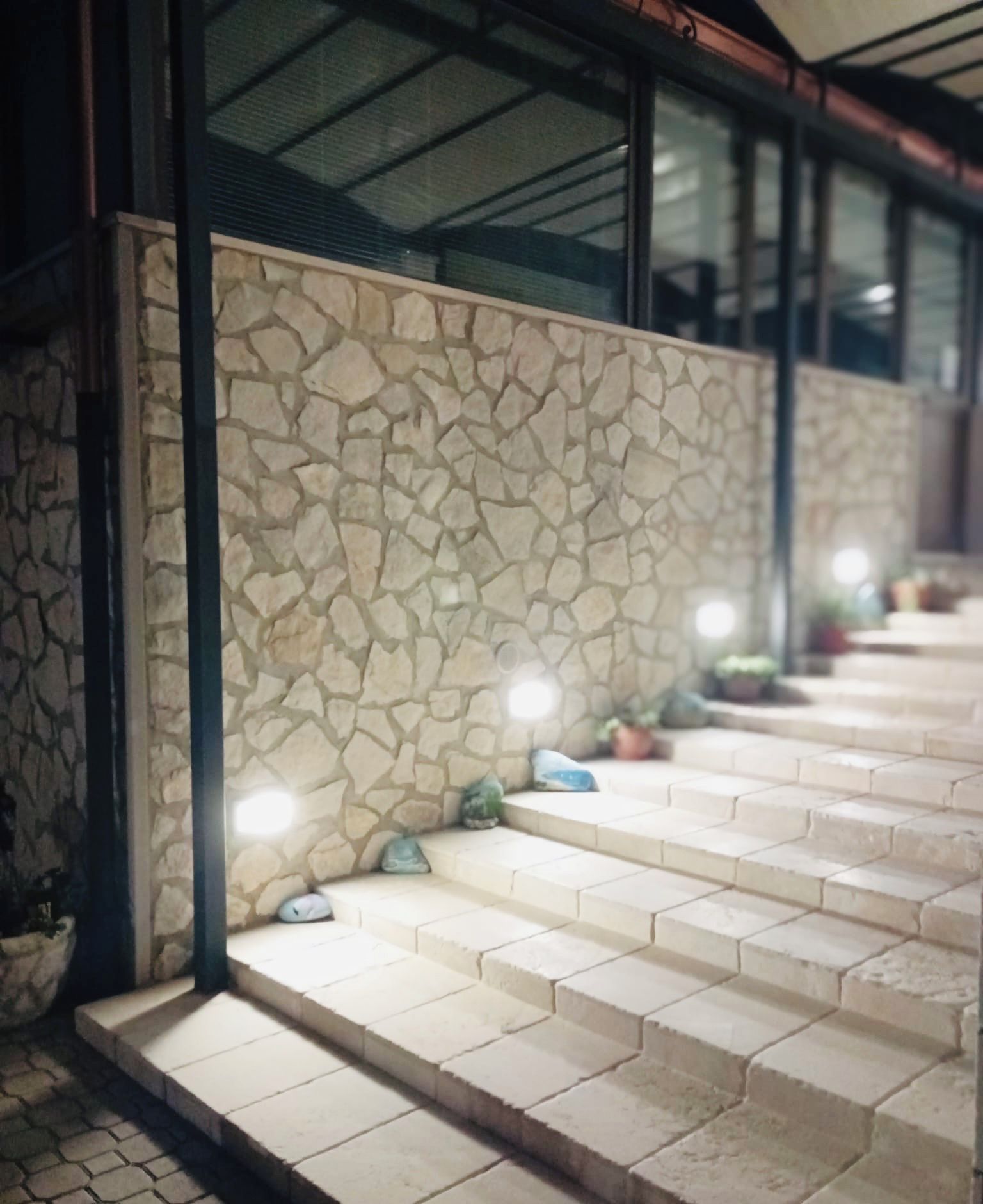 A stone wall with a textured pattern, leading to a set of steps with a light fixture above.