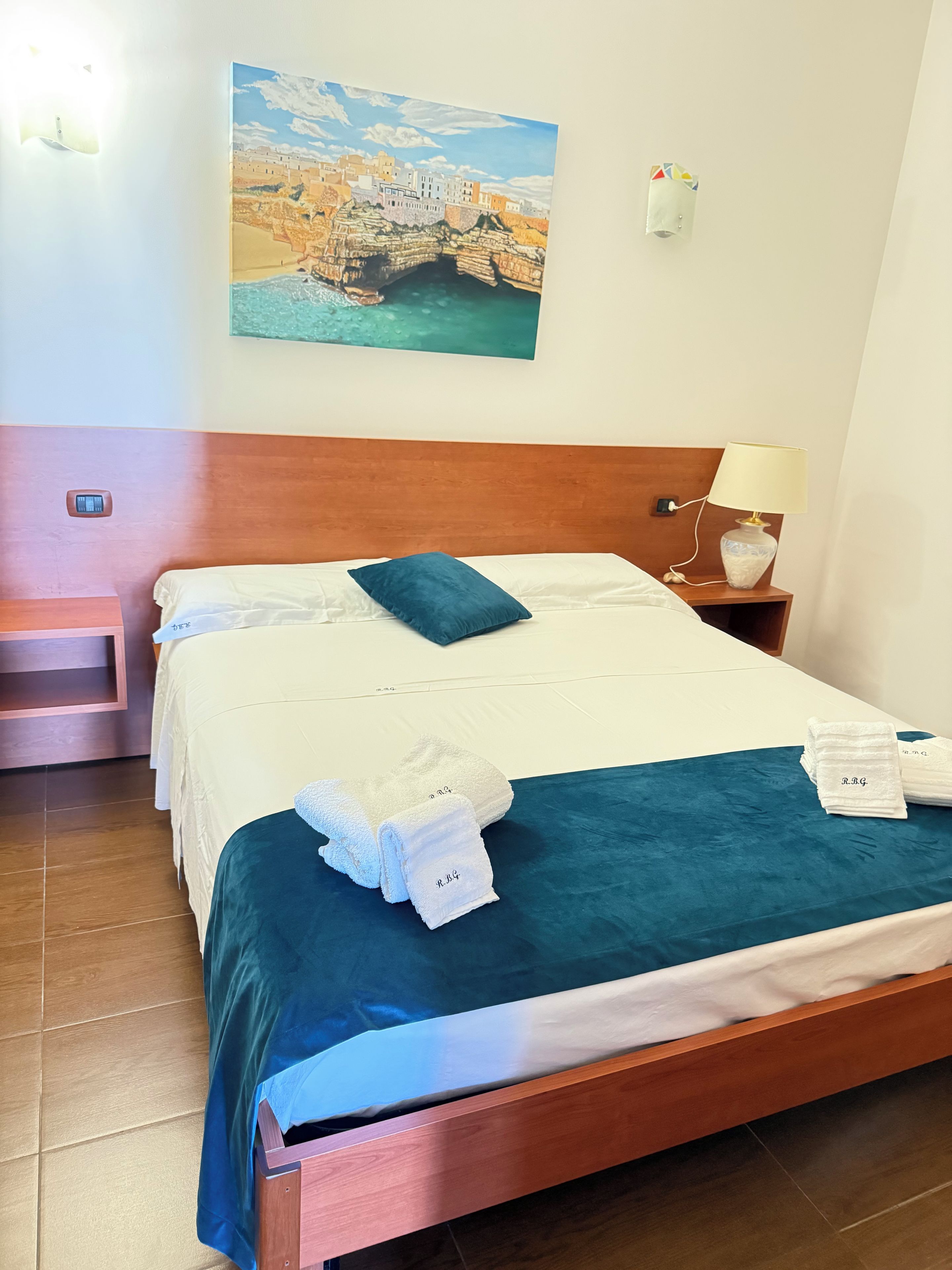 Een hotelkamer met een bed, een nachtkastje, een lamp en een schilderij aan de muur.