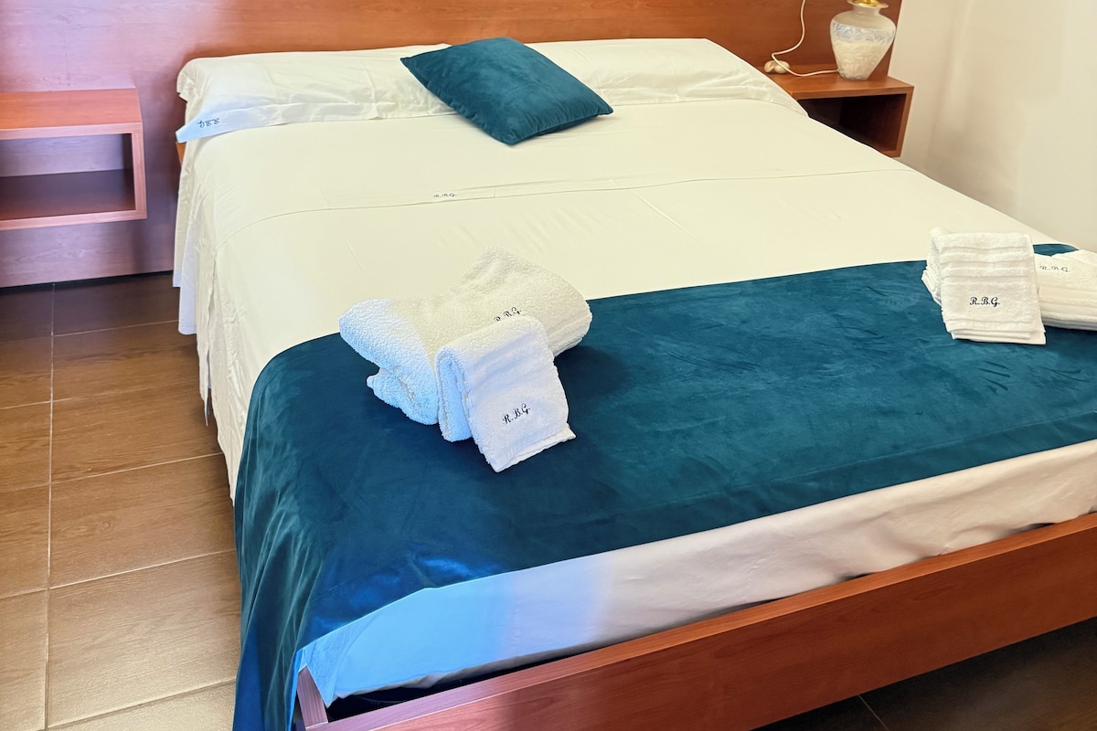 A hotel room with a bed, a nightstand, a lamp, and a painting on the wall.