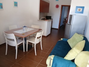 A compact living space with a dining table, chairs, a kitchenette, and a sofa with cushions.