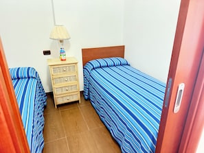 A small room with two beds, a wooden dresser, and a lamp.