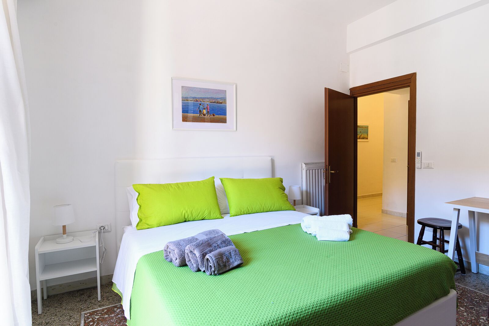 Quarto de hotel com cama, mesa de cabeceira, escrivaninha e porta que dá para outro cômodo.