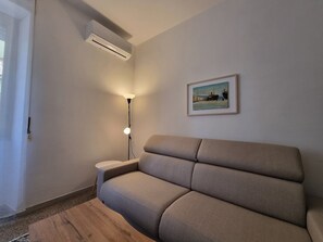 A living room with a sofa, a lamp, an air conditioner, and a framed picture on the wall. - Easy Metro Apartment Rome Boccea (Roma)
