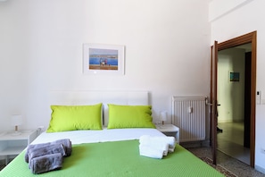 A hotel room with a bed, green bedspread, two pillows, a nightstand with a lamp, a picture on the wall, and a door leading to another room. - Easy Metro Apartment Rome Boccea (Roma)