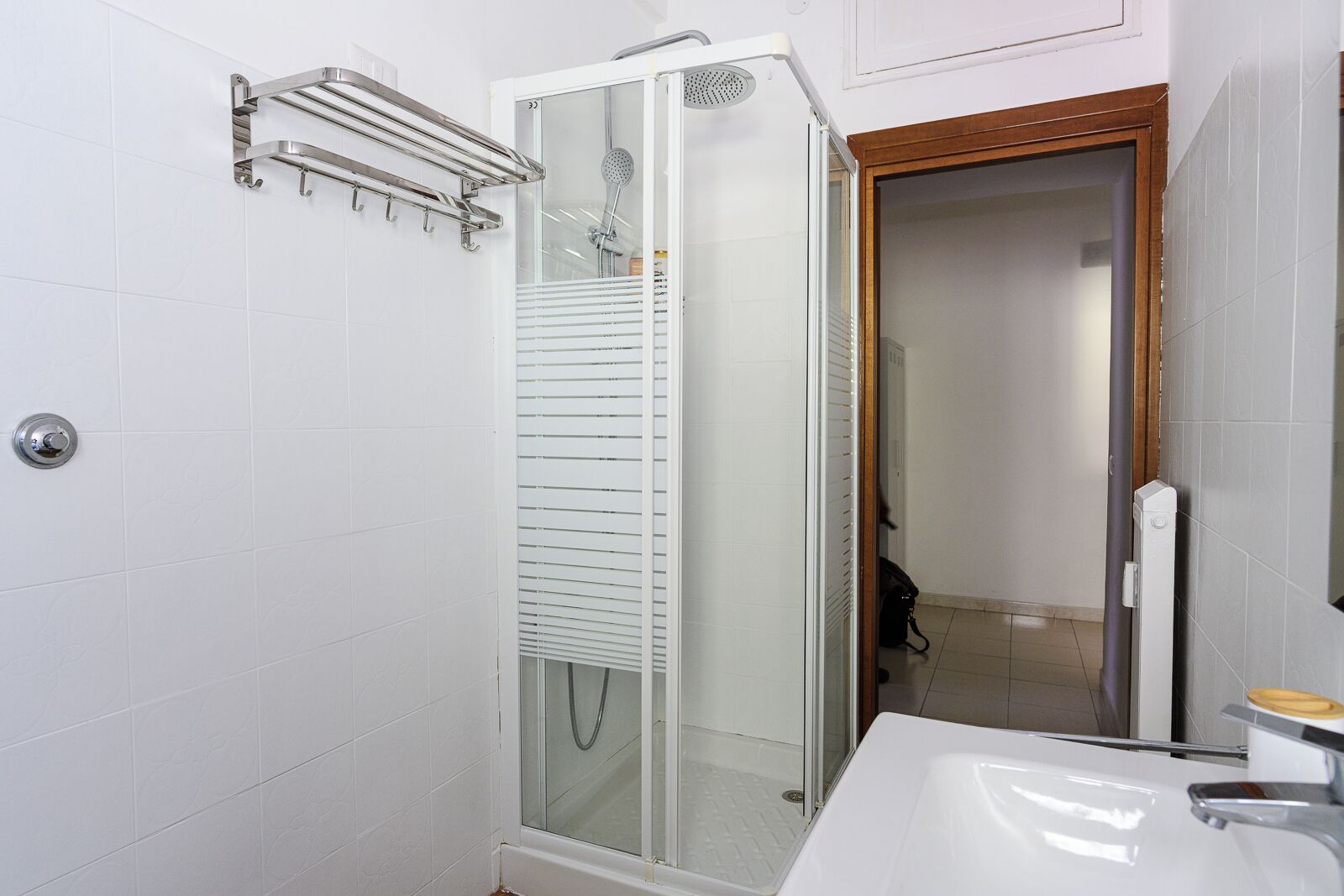 Ein Badezimmer mit einer gläsernen Duschkabine, einem weißen Waschbecken und einer Holztür.