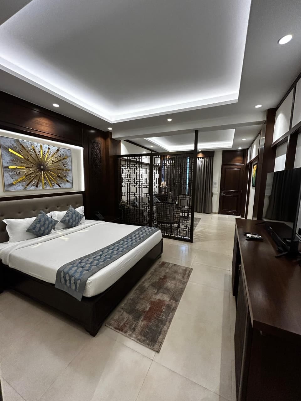 Quarto moderno com uma cama grande, televisão e um detalhe decorativo na parede.