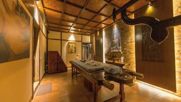 Quarto tradicional com teto de madeira, uma cama grande com cabeceira, um banco de madeira e uma prateleira fixada na parede.