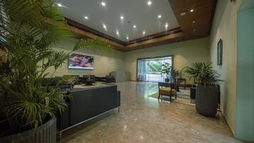 A reception area with a reception desk, seating, potted plants, and a large screen displaying content.
