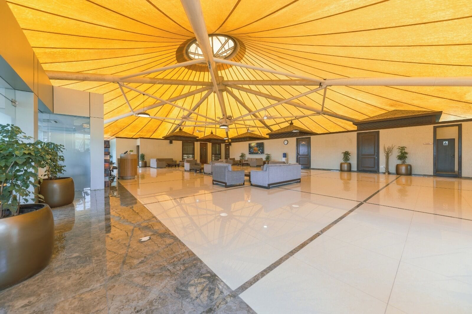 A spacious lobby with a high ceiling and a central circular skylight, featuring a reception desk, seating areas, and potted plants.