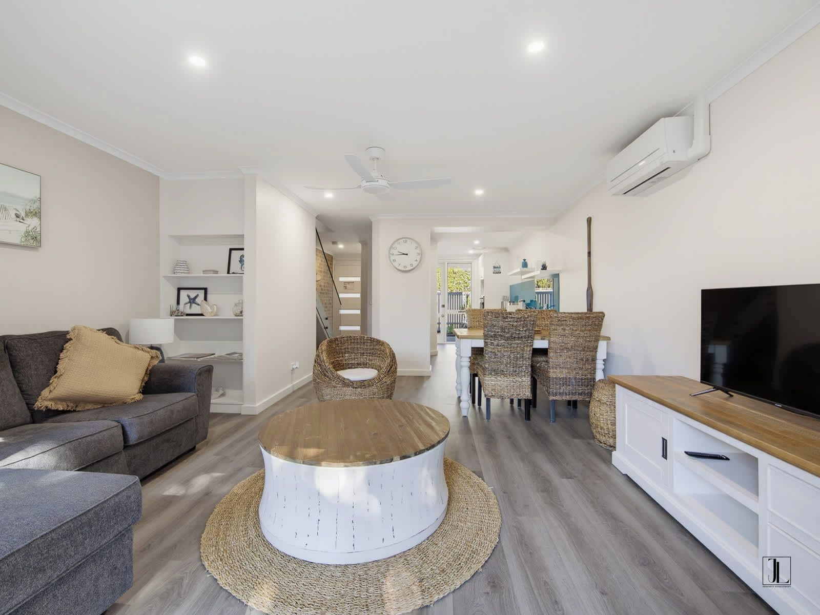 A modern living room with a sofa, round coffee table, wicker chairs, a dining table, and a TV.