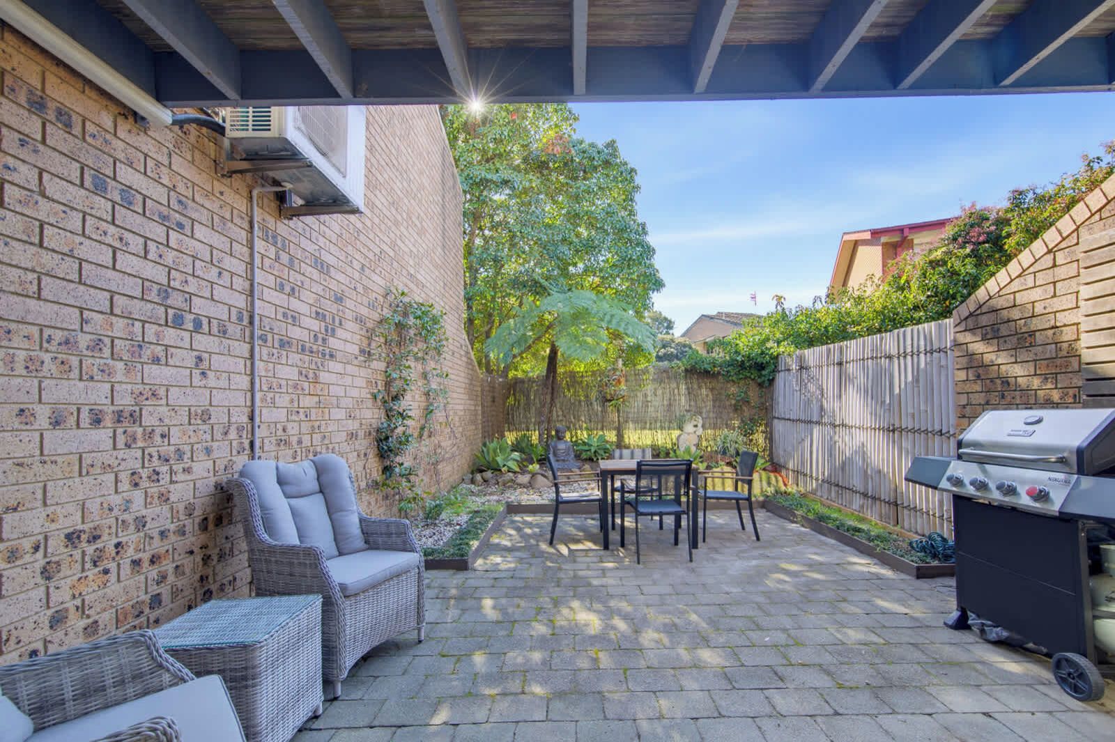 A patio with a brick wall, wicker furniture, a grill, and a tree.