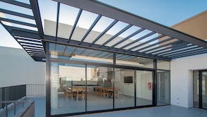 A modern interior with a glass wall, a dining area with wooden furniture, and a metal ceiling structure. - Corporate Stays First del Sol - 104 (Asunción)