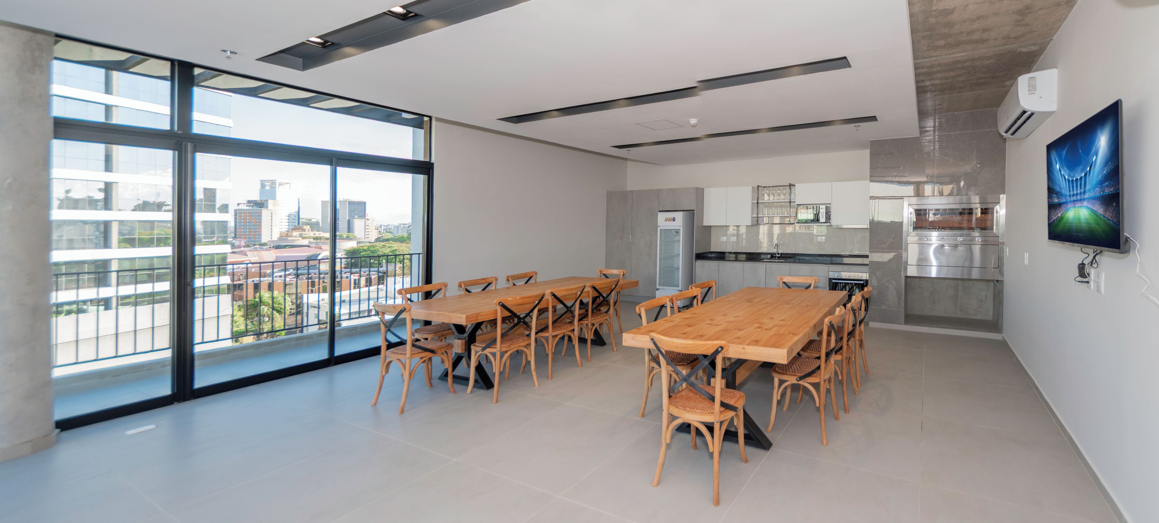 Una cocina moderna con horno empotrado, un ventanal grande y un comedor con mesas y sillas de madera.