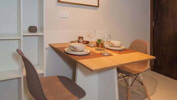Un comedor con una mesa lista para dos personas, dos sillas, un cuadro en la pared y una estantería blanca con objetos.