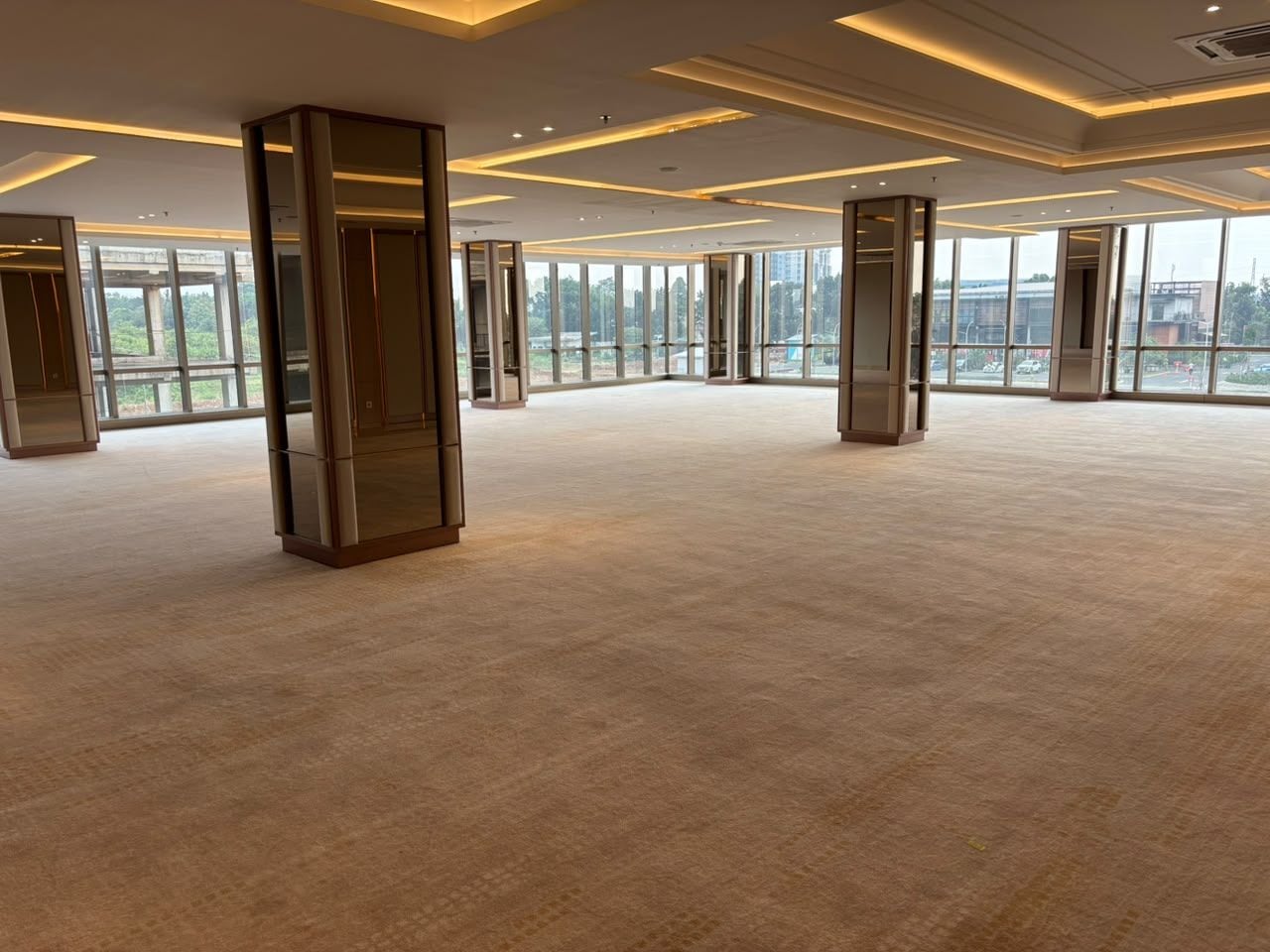 A spacious room with a high ceiling, large windows, and a carpeted floor.