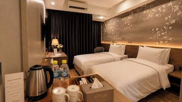 Habitación de hotel con dos camas, un escritorio con hervidor, botellas de agua y una caja de pañuelos.