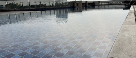 An indoor swimming pool with clear water, surrounded by a tiled deck and a glass railing.