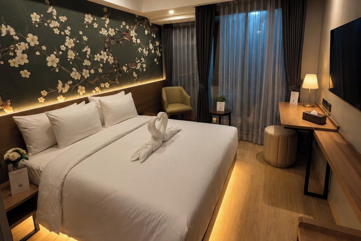 A hotel room with a large bed, a desk, a chair, a TV, and a wall with a floral design.