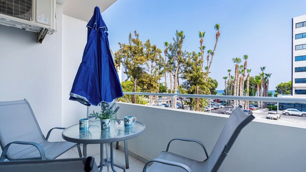 A balcony with a table, chairs, and a blue umbrella.