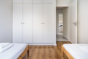 A bedroom with two beds, a wardrobe, and a kitchen visible through an open door. - Limassol Seafront Family Suite Beachfront Stay (Lemesos)