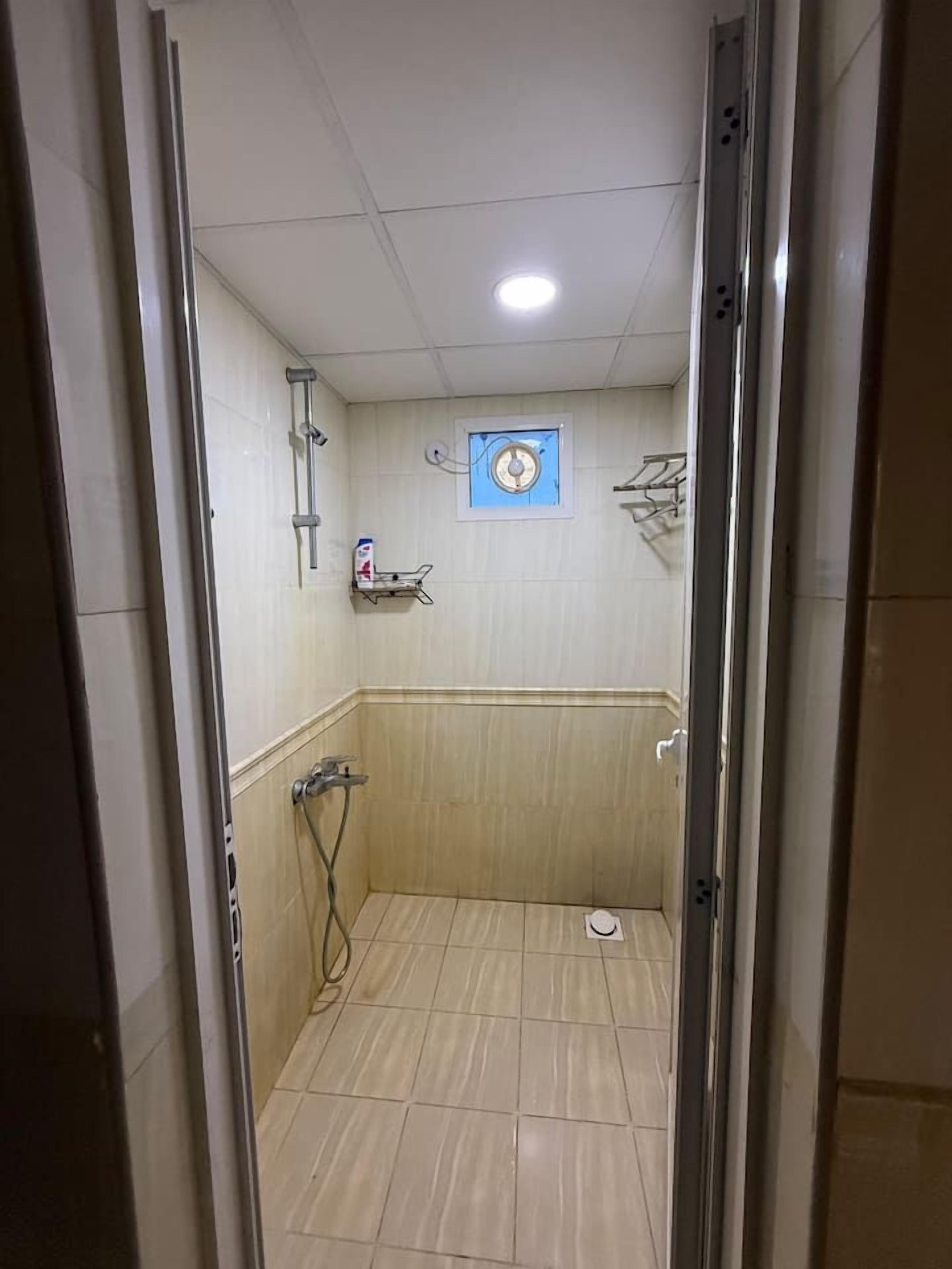 A narrow, tiled shower area with a showerhead and a wall-mounted shelf.