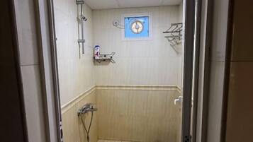 A narrow, tiled shower area with a showerhead and a wall-mounted shelf.