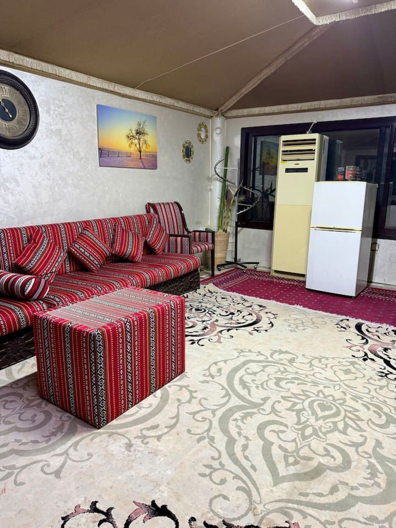 A living room with a sofa, ottoman, and patterned rug.