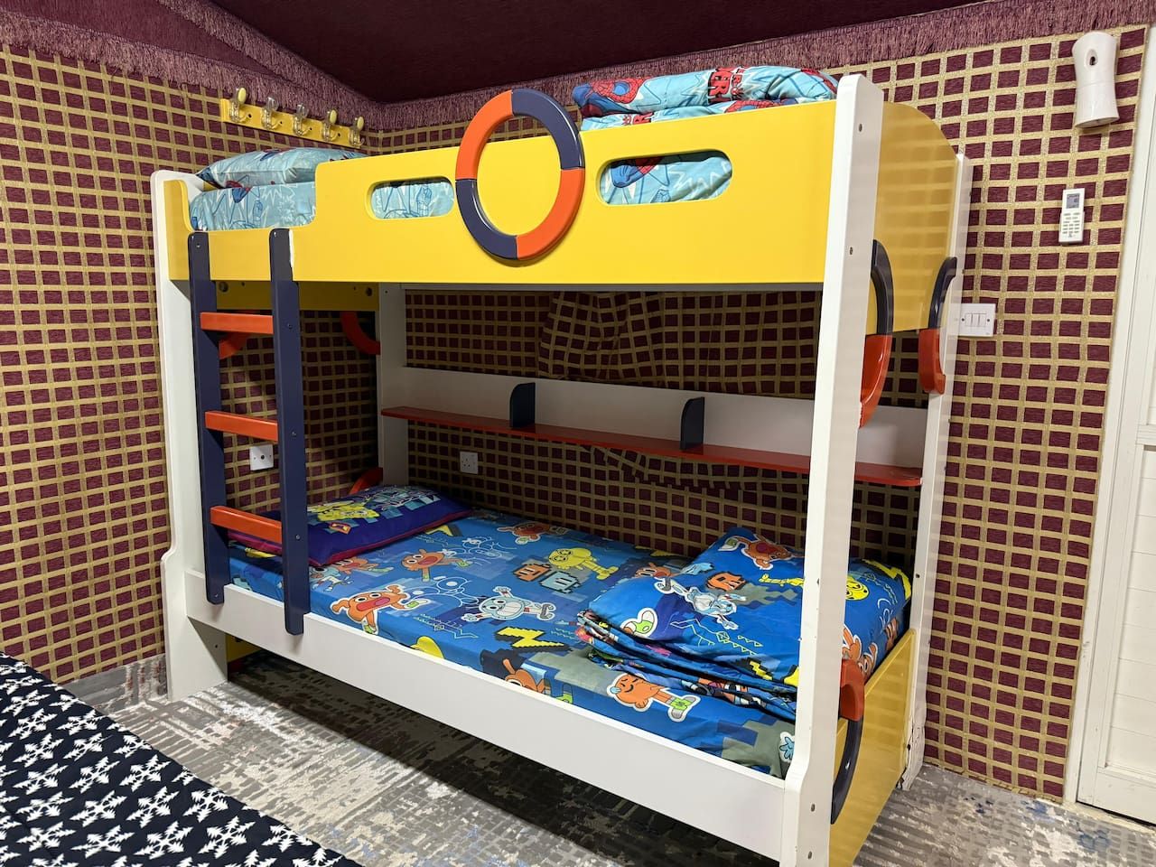 A bunk bed with a circular decoration on the headboard, a patterned wall, and a small white object on the wall.