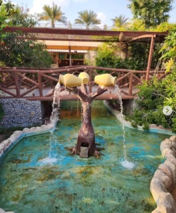 Una fuente de agua con estructura arbórea y un puente al fondo.