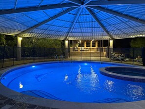 A swimming pool with a covered area and a hot tub, surrounded by a fence and a patio with seating.