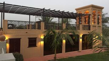 A two-story building with a balcony, palm trees, and a well-lit entrance.