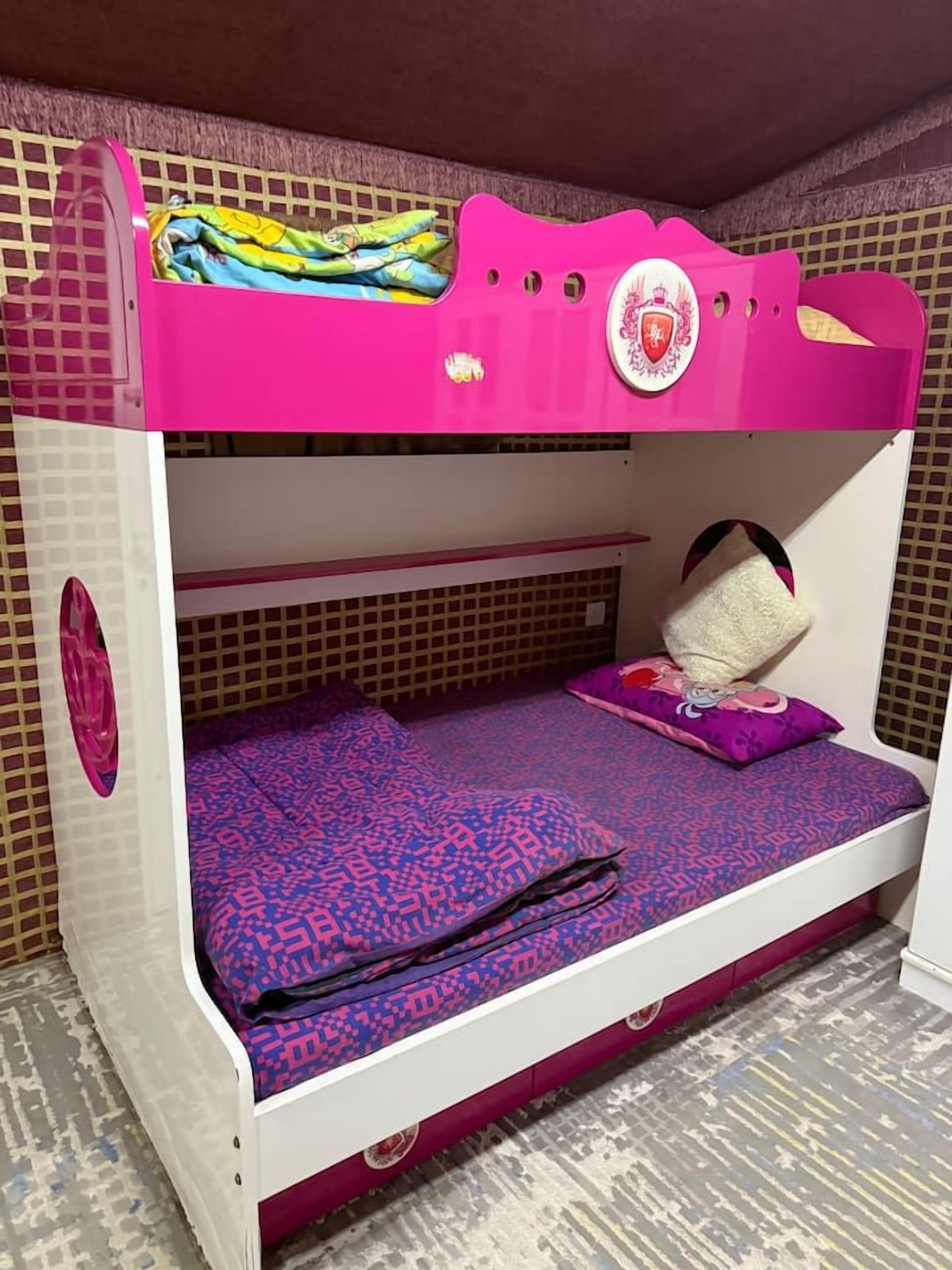 A bunk bed with a pink top bunk and a lower bunk with a patterned bedspread.
