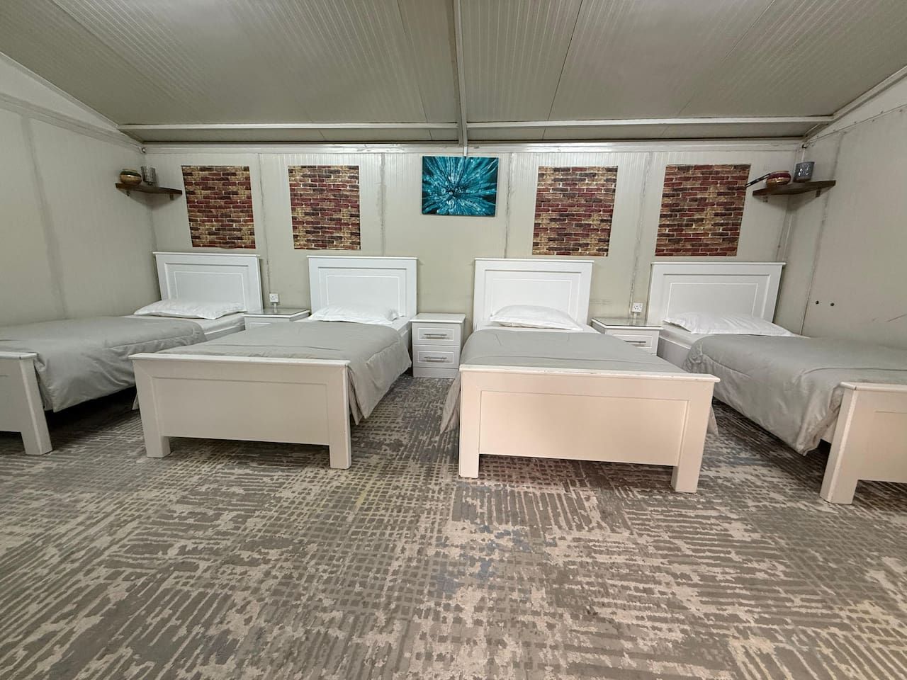 A hotel room with four beds arranged in a square layout, a patterned carpet, and a brick wall accent.