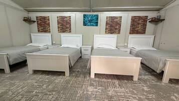 A hotel room with four beds arranged in a square layout, a patterned carpet, and a brick wall accent.