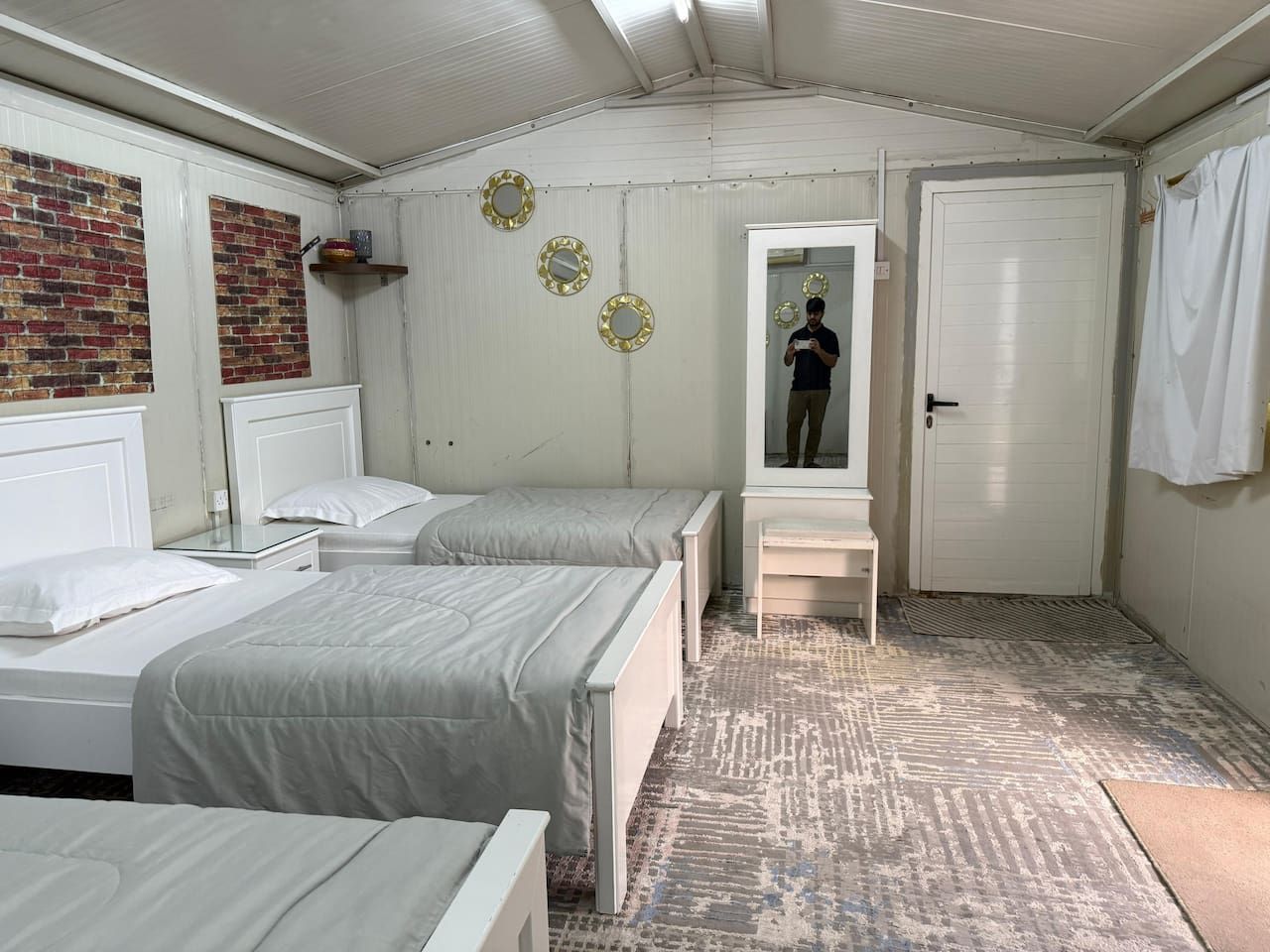 A room with two beds, a bench, a door, and a mirror.