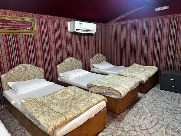 Habitación de hotel con tres camas, alfombra estampada y unidad de aire acondicionado.