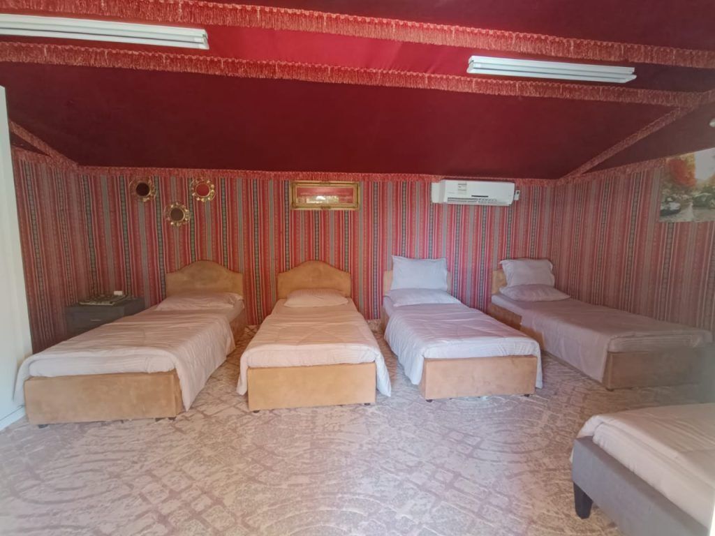 A room with four beds arranged in a row, a red ceiling, and striped wallpaper.