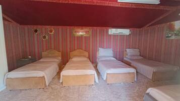 A room with four beds arranged in a row, a red ceiling, and striped wallpaper.