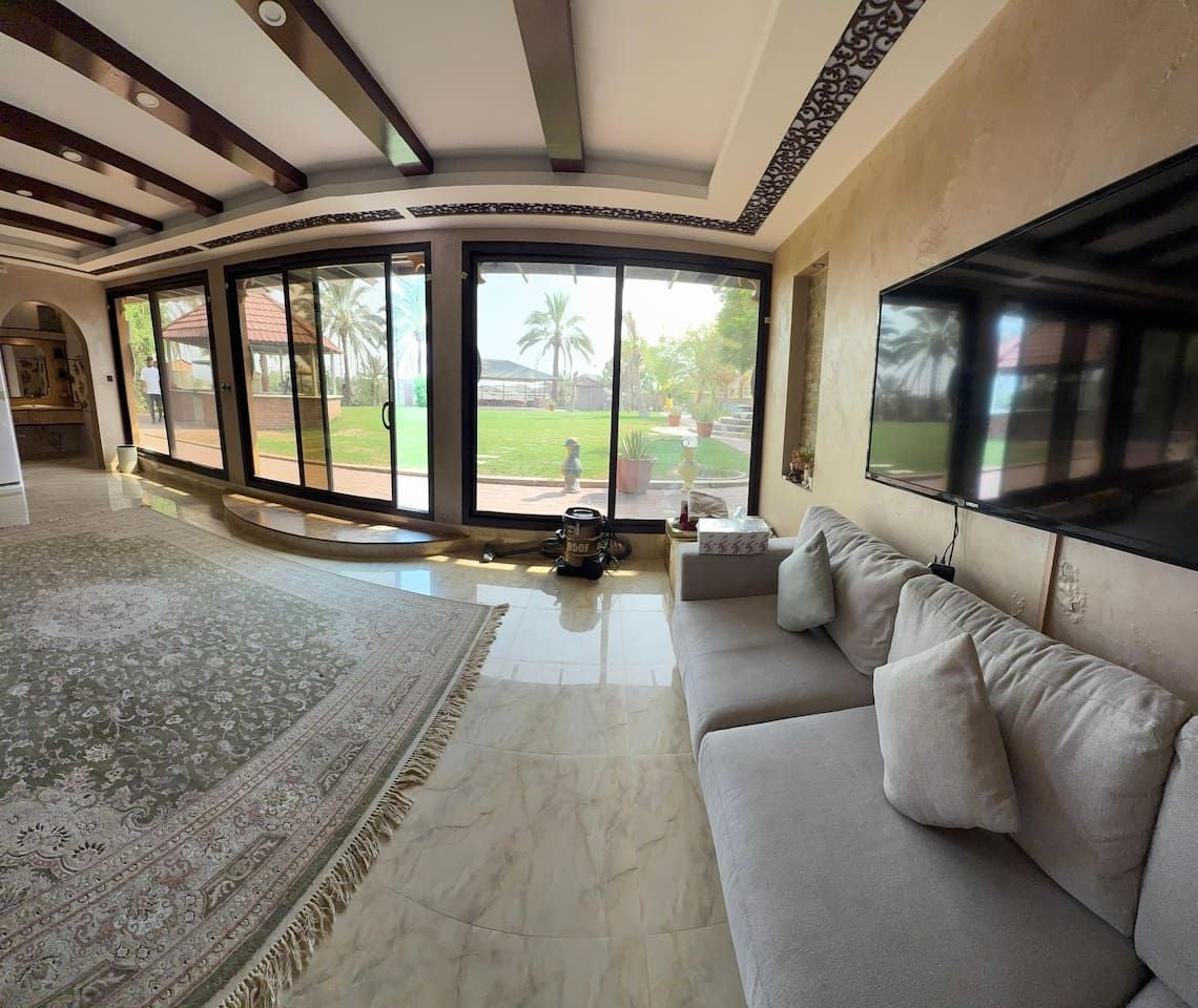 A spacious living room with a large sofa, a television, and a view of a garden through large windows.