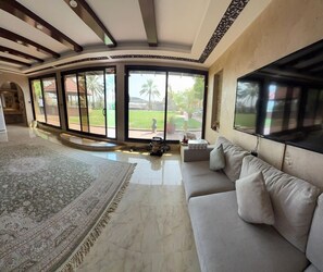 Amplia sala de estar con un sofá grande, un televisor y vistas a un jardín a través de grandes ventanales.
