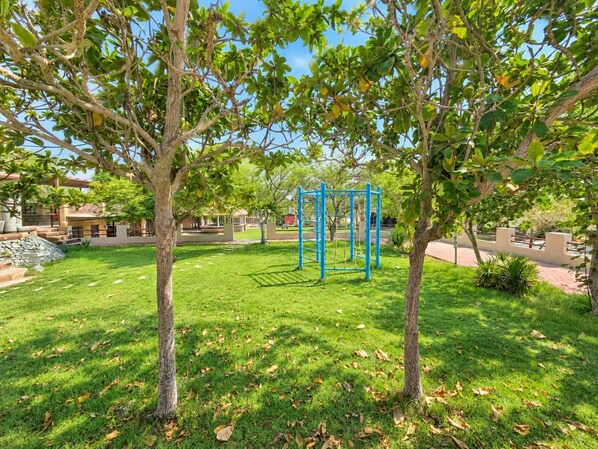 A park with a playground, trees, and a building in the background.